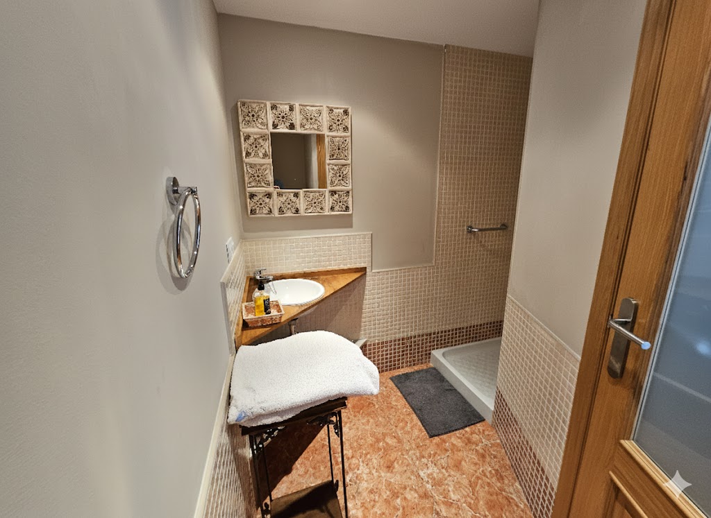 Baño habitación doble con ducha a ras de suelo, mueble de madera con lavabo, espejo decorativo y acabados en tonos tierra