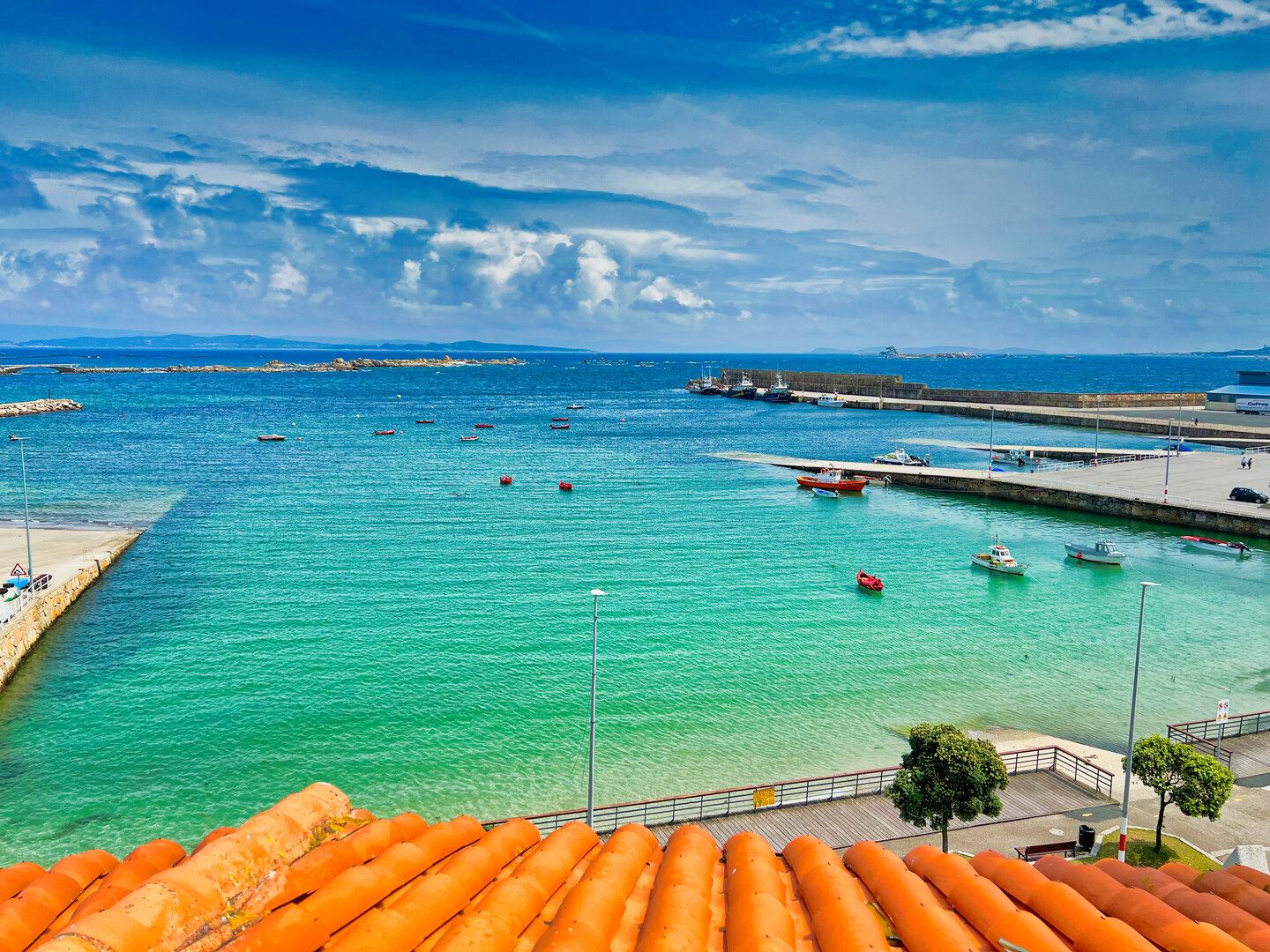 Vista panorámica desde la terraza del ático Illas Atlánticas al puerto de Aguiño con aguas turquesas y barcas tradicionales en la Ría de Arousa, Galicia