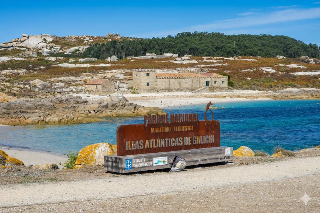 Cartel oficial del Parque Nacional Illas Atlánticas de Galicia en la Isla de Sálvora con playa de arena blanca, aguas cristalinas turquesas y edificios históricos